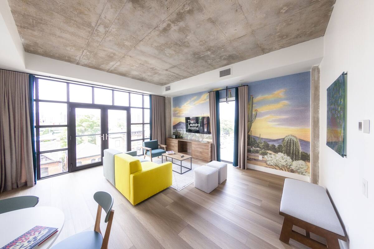 Un salón amplio con un sofá amarillo, una mesa de centro de madera y un mural que representa un paisaje desértico.