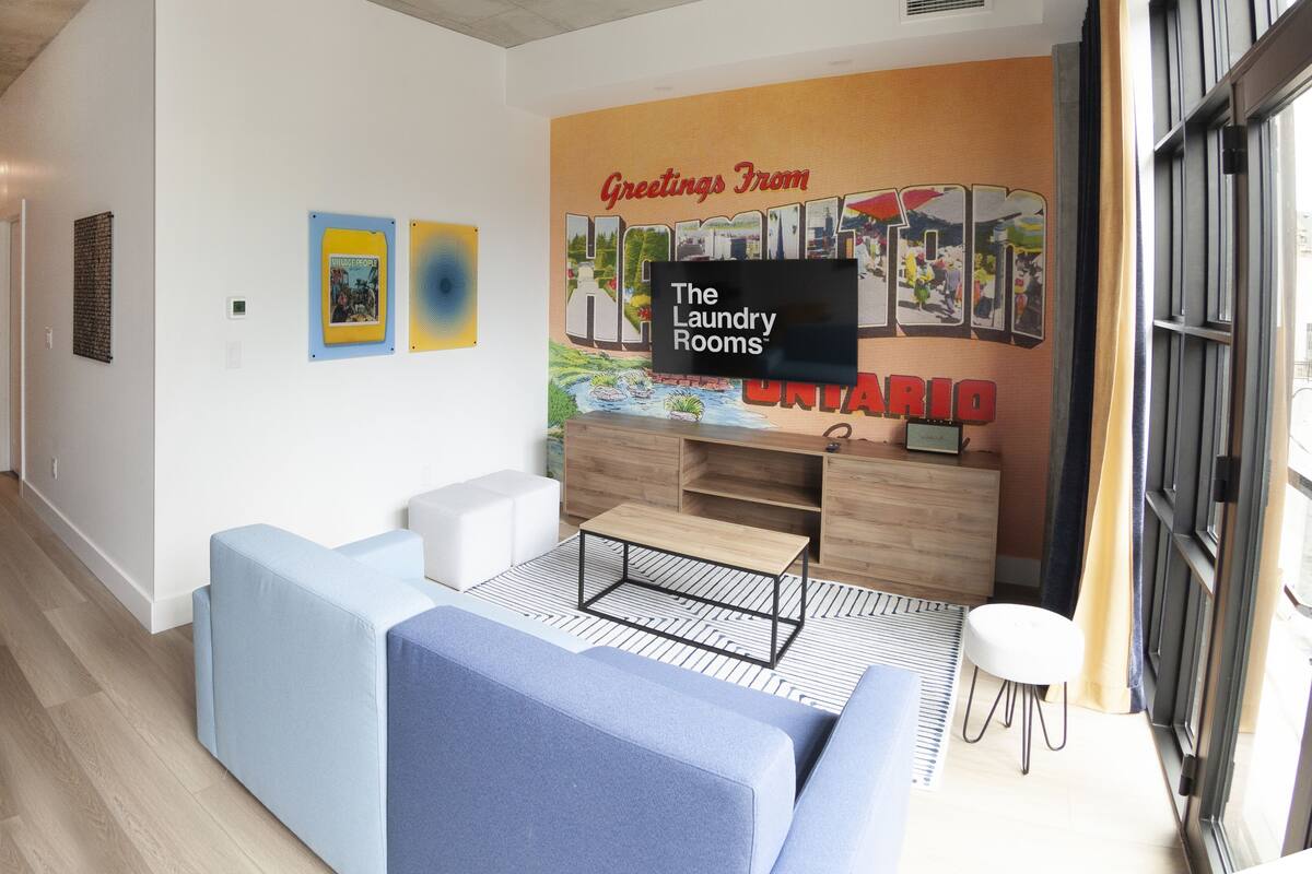 Una sala moderna con un televisor de pantalla plana grande, un sofá, una mesa de centro y un mural en la pared.