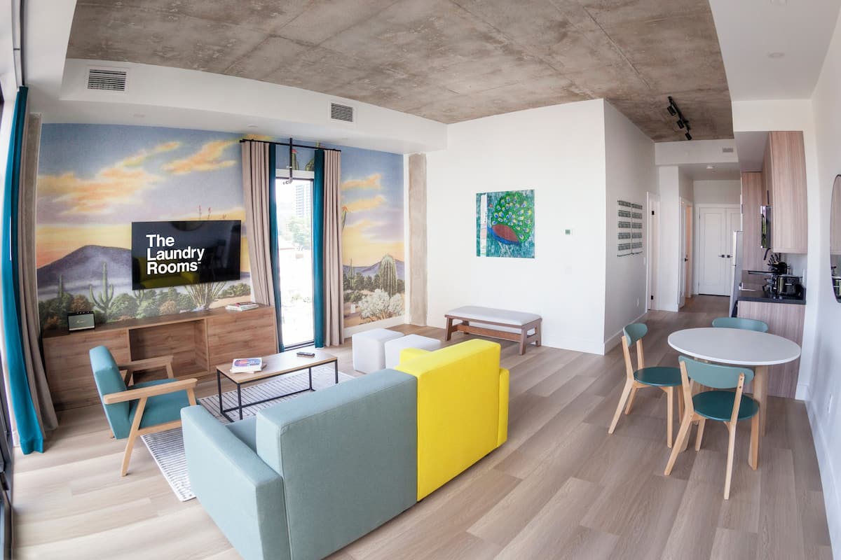 Una sala de estar moderna con un sofá, sillas, una mesa de centro y una pantalla de televisión que muestra 'The Laundry Rooms'.