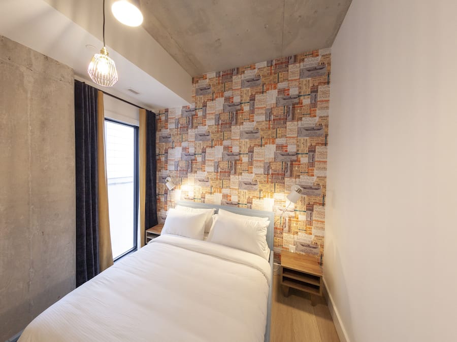 A bedroom with a large bed, a patterned wall, a window with curtains, and a hanging light fixture.