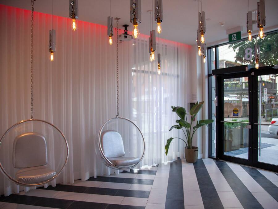 A hotel lobby with two hanging chairs, a potted plant, and a view of the street through the entrance.