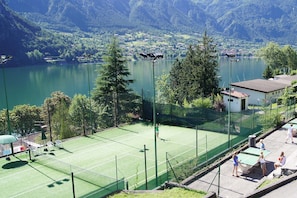 A tennis court with a net, surrounded by a fence, and overlooking a lake with a mountainous backdrop. - In Seenähe mit Panoramablick (Tre Capitelli)