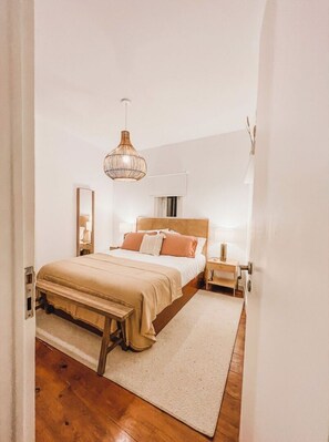 A bedroom with a bed, bedside tables, a hanging light fixture, and a door.