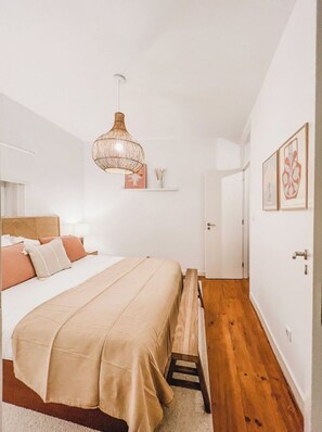 A bedroom with a bed, bedside table, lamp, hanging light fixture, and a door.
