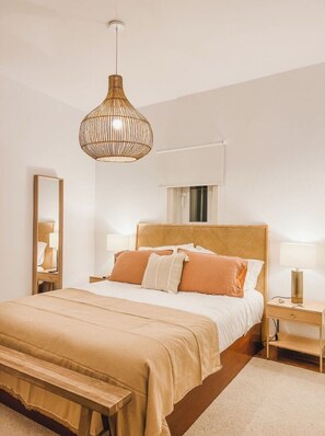 Un dormitorio con cama, mesitas de noche, un banco, una lámpara colgante y un espejo.