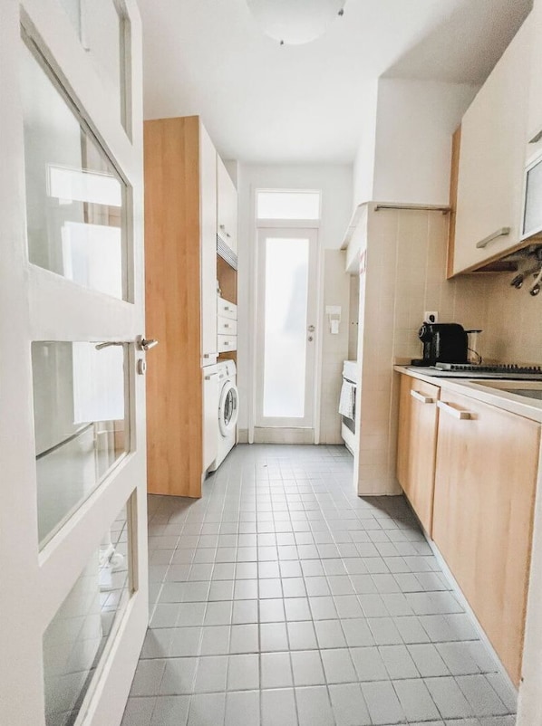 A narrow hallway with a washing machine, a door, and a kitchen area with cabinets and a stove.