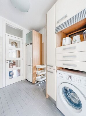 Un cuarto de lavandería con lavadora, un tendedero y un armario con electrodomésticos de cocina.