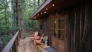 Une cabane en bois dotée d’une terrasse, de deux fauteuils à bascule et d’une porte avec des panneaux de verre.