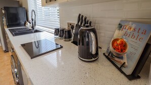 Een moderne keuken met een aanrecht, een waterkoker, een koffiezetapparaat, een messenblok en een boek getiteld 'The Pasta Bible'.