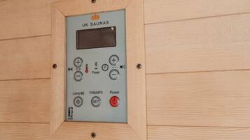 Panel de control de sauna con varios botones y una pantalla digital, fijado a una pared de madera.
