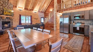 Une cabane en bois spacieuse, comprenant un coin repas, une cuisine et une cheminée en pierre.