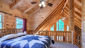 Une chambre dans une cabane en bois, avec un grand lit, un ventilateur de plafond et une vue sur l’extérieur.