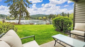 A patio with a glass table and two chairs, overlooking a lake and forested hills. - Waterfront Condo, Flathead Lake and Mountain Views! (Bigfork)