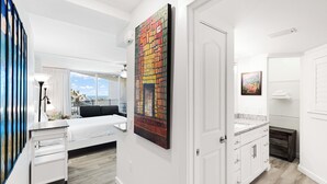 Quarto de hotel moderno com uma janela grande, uma cama, um penteou branco e uma pintura de uma paisagem urbana.