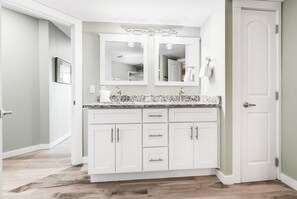 A bathroom with a white vanity, two mirrors, a sink, and a door.