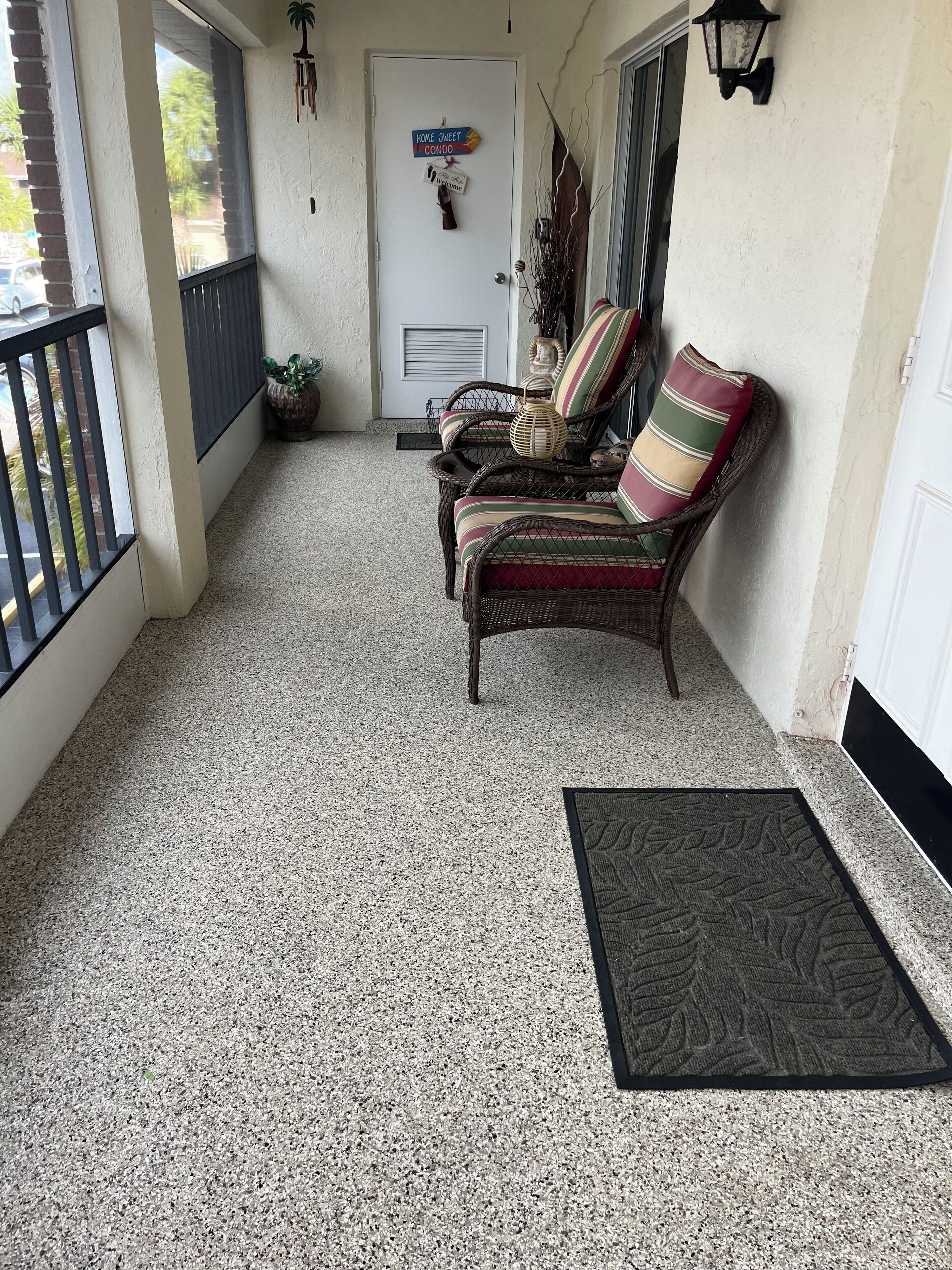 A covered porch with a wicker chair, a doormat, and a door with a welcome sign.