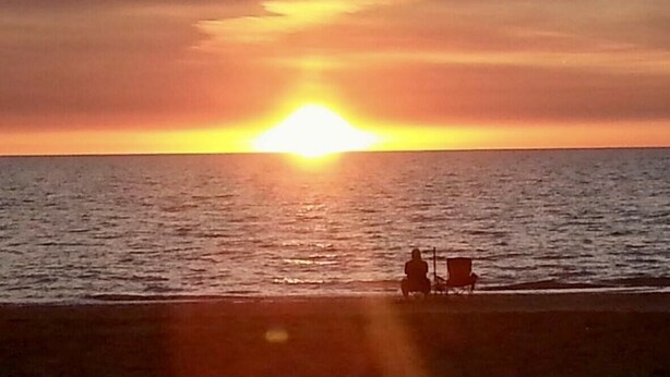 A sunset over the ocean with two people sitting on chairs facing the water. - Your piece of Paradise at Palm Manor Condo (Englewood)