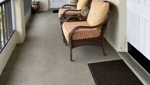 A covered porch with wicker furniture, a door labeled "1-203", and a decorative sign. - Your piece of Paradise at Palm Manor Condo (Englewood)