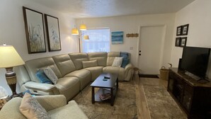 A living room with a sectional sofa, a coffee table, a TV stand, and artwork on the walls. - Your piece of Paradise at Palm Manor Condo (Englewood)