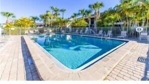 A swimming pool with a tiled deck, surrounded by palm trees and a clear sky. - Your piece of Paradise at Palm Manor Condo (Englewood)
