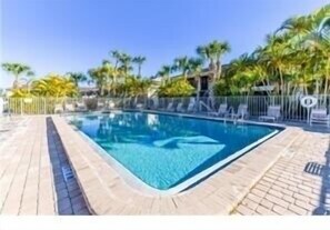 Relax by the pool surrounded by a paved deck and a low fence.