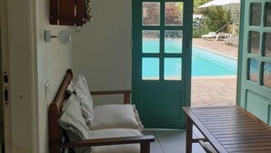 A room with a wooden bench, a small table, and a door leading to a pool area. - CHARMING HOUSE WITH POOL 5 MINUTES FROM THE BEACH! (LE GOSIER)