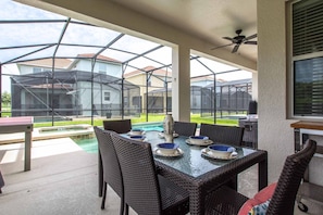 An outdoor patio with a glass table and wicker chairs, overlooking a swimming pool and neighboring houses. - 6BR Disney Pool Home | 3 King Bedrooms | Private Pool & Spa | Sleeps 14 (Kissimmee)