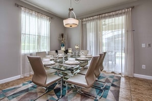 A dining area with a glass table set for six, surrounded by six chairs. - 6BR Disney Pool Home | 3 King Bedrooms | Private Pool & Spa | Sleeps 14 (Kissimmee)