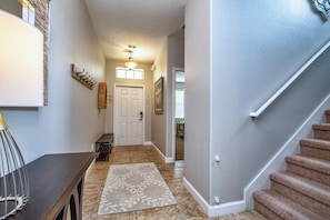 A hallway with a door, a staircase, and a patterned rug. - 6BR Disney Pool Home | 3 King Bedrooms | Private Pool & Spa | Sleeps 14 (Kissimmee)