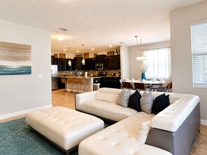 Een moderne woonkamer met een hoekbank, poefs en een eethoek met een tafel en stoelen.
