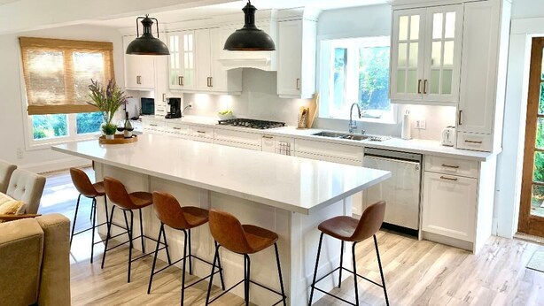 Una cocina amplia con una isla grande, armarios blancos e iluminación colgante moderna.