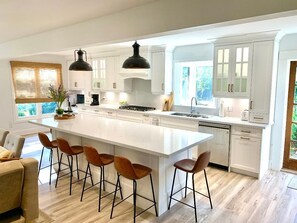 Une cuisine spacieuse dotée d’un grand îlot central, de meubles blancs et d’un éclairage moderne suspendu au plafond.