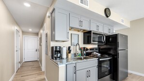 A modern kitchen with grey cabinets, a stainless steel refrigerator, a microwave, and a stove. - Sandcastle Condominiums Unit 532 (Port Aransas)