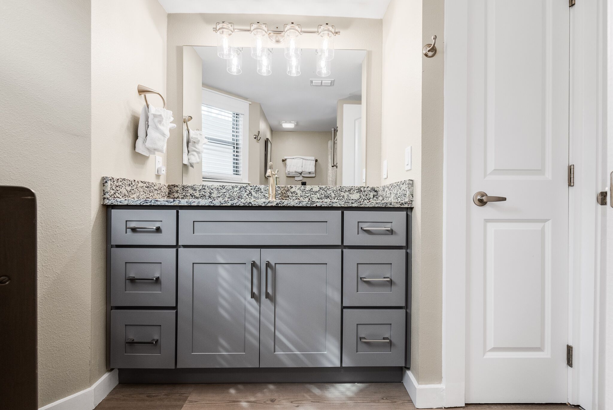 Une salle de bain avec un comptoir en granit, un grand miroir et une porte blanche.