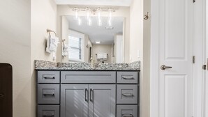A bathroom with a granite countertop, a large mirror, and a white door. - Sandcastle Condominiums Unit 532 (Port Aransas)