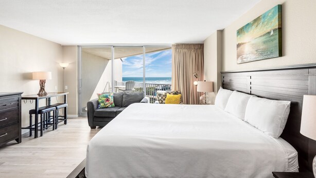A hotel room with a large bed, a desk with chairs, a sofa, and a view of the ocean. - Sandcastle Condominiums Unit 532 (Port Aransas)