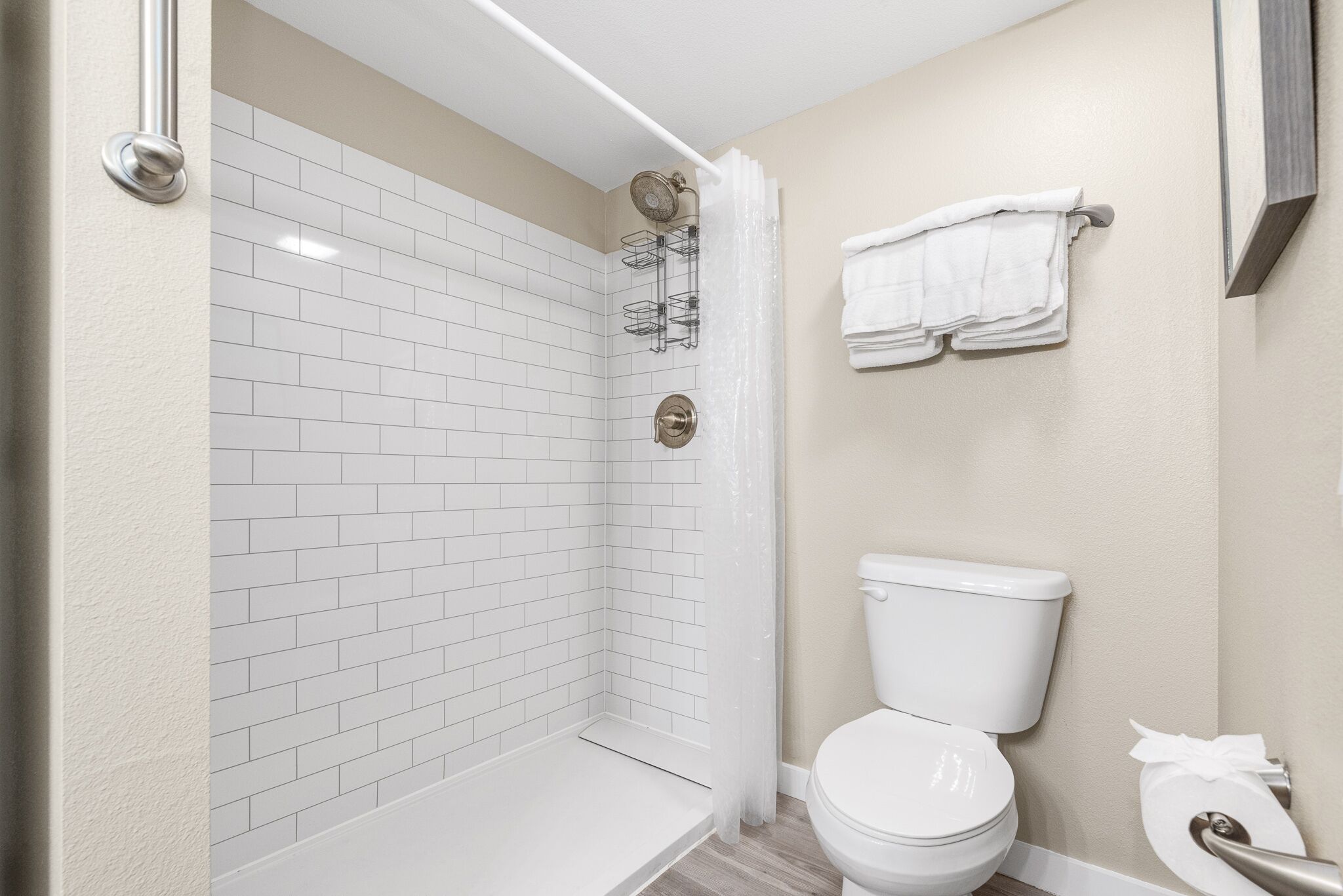 Een badkamer met witte betegelde wanden, een wit toilet en een douchecabine met een glazen deur.