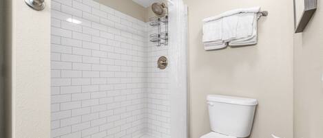 Een badkamer met witte betegelde wanden, een wit toilet en een douchecabine met een glazen deur.
