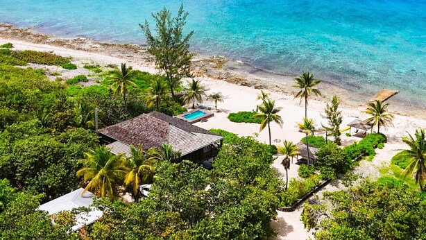 An aerial view of a beachside property with a swimming pool, palm trees, and a small building. - Featherstone - Upstairs Beach Front Apartment (Tibbett's Turn)