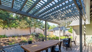 Un patio couvert avec une table et des chaises en bois, un barbecue et un abri de jardin en arrière-plan.