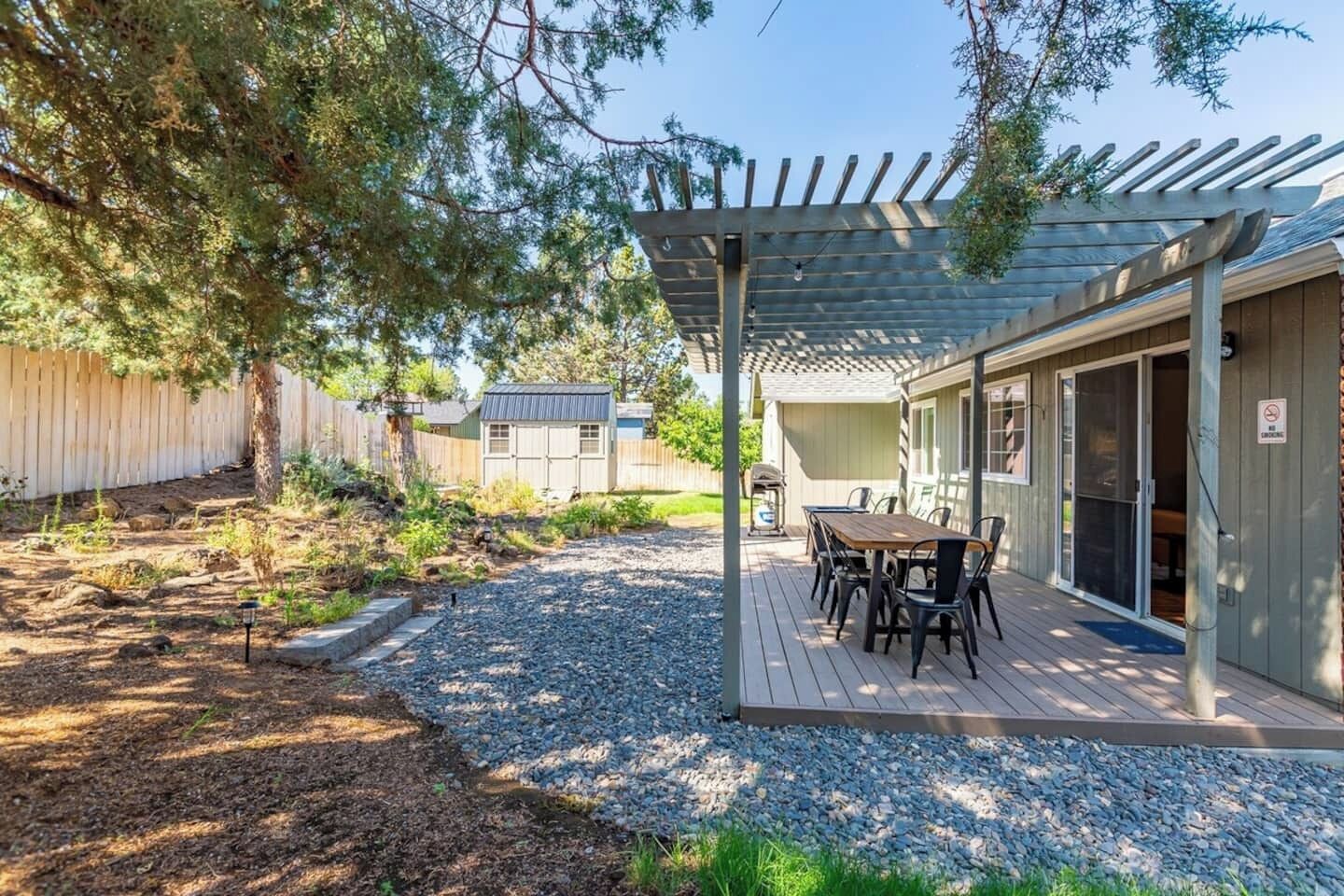 A covered patio with a table and chairs, a pergola, and a wooden fence in the background.