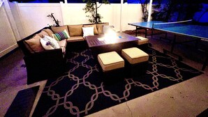 An outdoor patio area with a sofa, ottomans, a table, and a ping pong table.