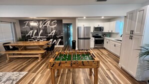 A modern kitchen with white cabinets, a stainless steel refrigerator, an oven, and a microwave. There's a wooden foosball table in the center.