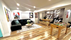 A modern living room with a black sofa, round coffee table, wooden flooring, and a foosball table.
