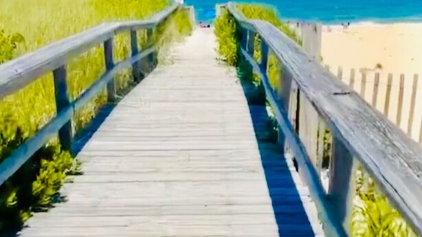 Ein hölzerner Steg führt zu einem Strand mit freiem Blick auf das Meer.