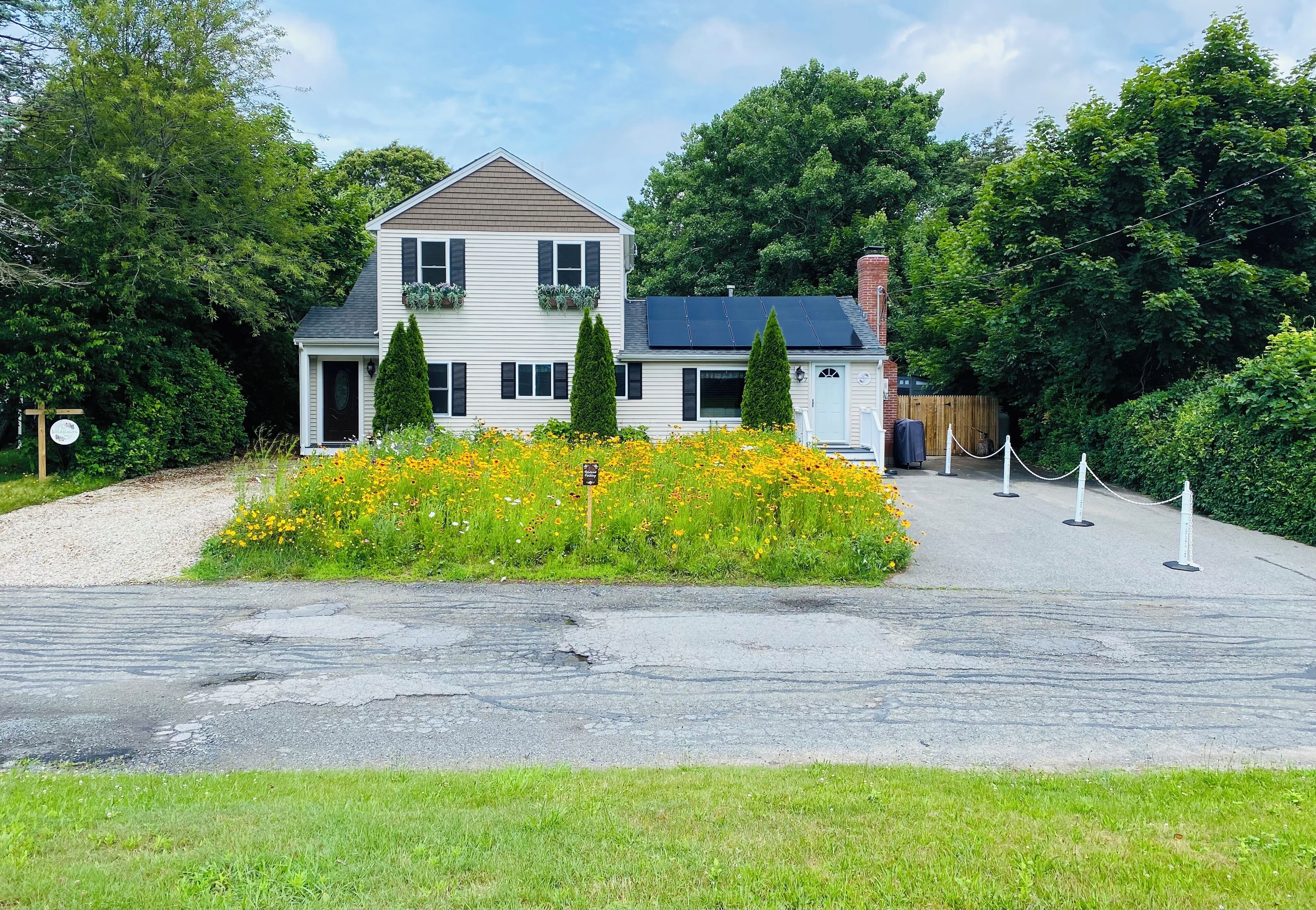 Une maison à deux étages avec un toit en pente, un porche à l’avant et une petite construction en bois sur le côté droit.