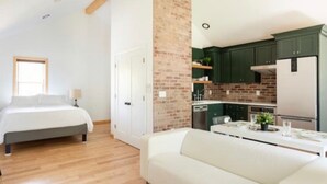 Ein modernes Schlafzimmer mit Bett, Nachttisch und Beistelltisch. Es gibt eine Küchenzeile mit grünen Schränken, einem Kühlschrank und einer Arbeitsplatte.