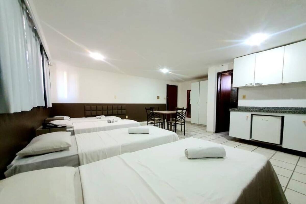 Une chambre d’hôtel avec quatre lits simples, une petite table à manger et un coin cuisine.