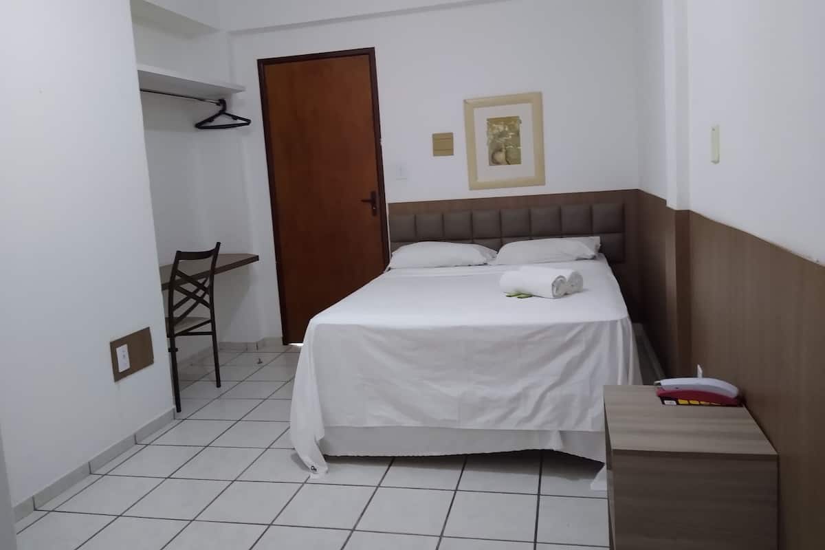 Une petite pièce propre, avec un lit, une chaise, un bureau et une porte.