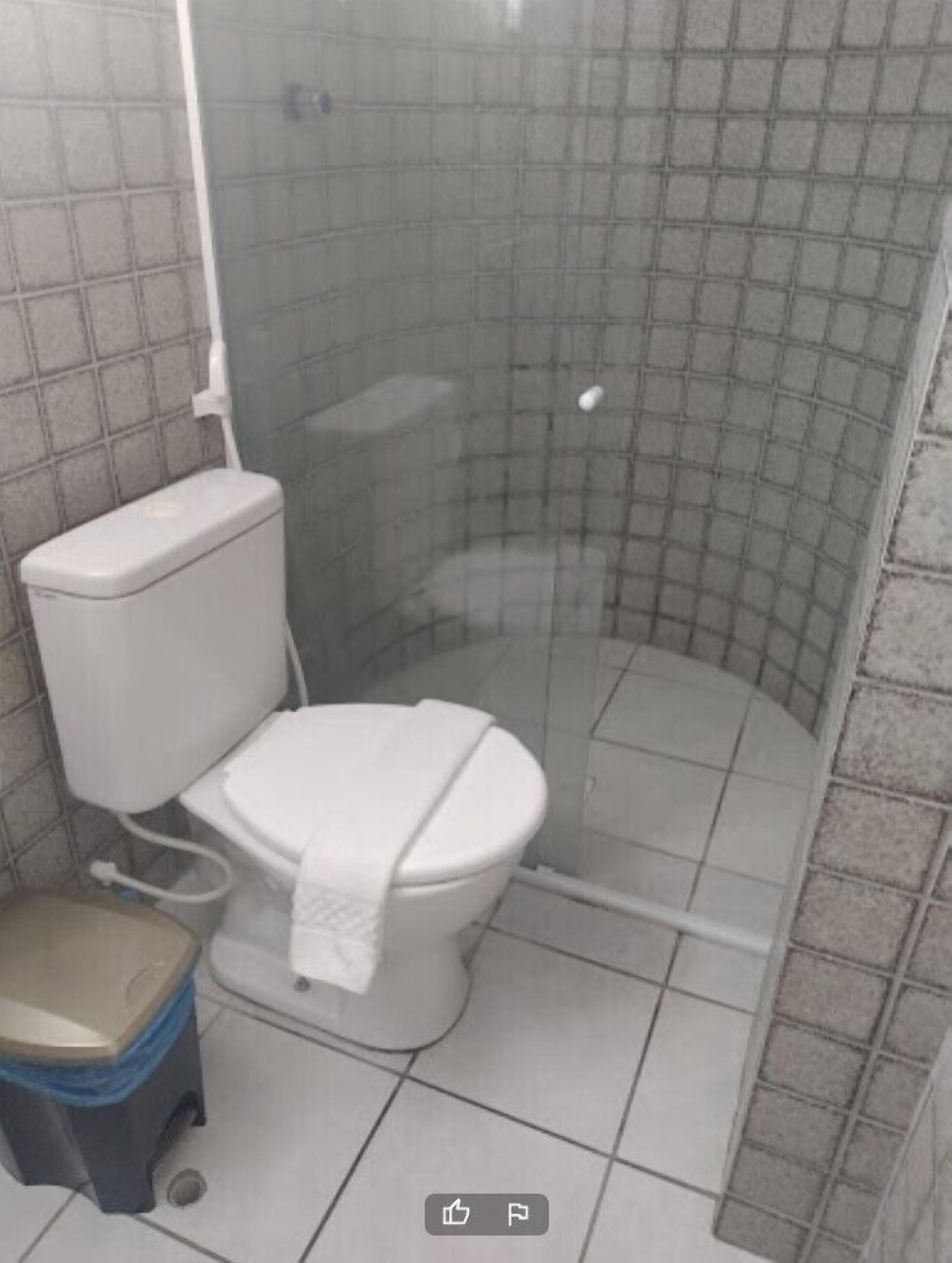 Un baño con inodoro, cabina de ducha y un taburete pequeño.